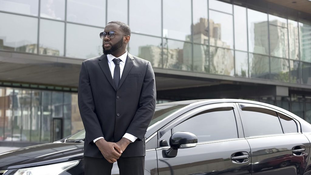 A licensed Close Protection guard waiting by a car outside an office building
