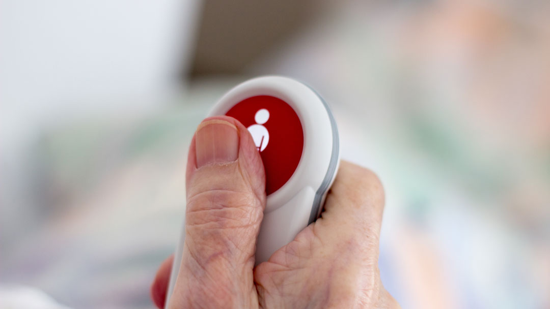 Close up of an elderly patient's hand using a Capricorn Installations Nurse Call button